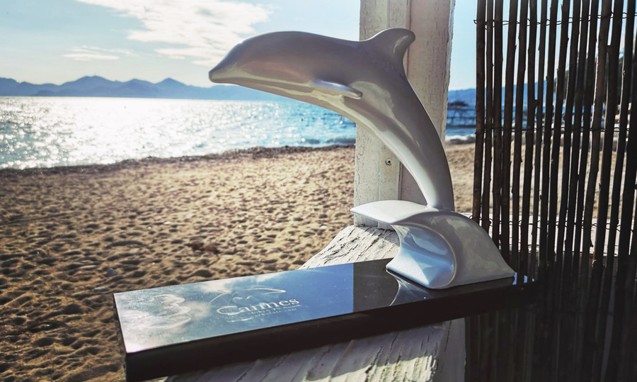 A 'White Doplphin' Grand Prix Award on a beach with a bright blue Mediterranean Sea in the background